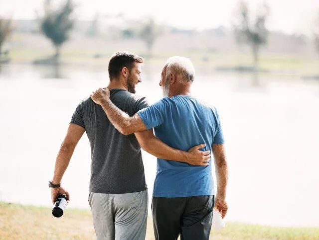 Senior father and adult son smiling as they walk together outside.