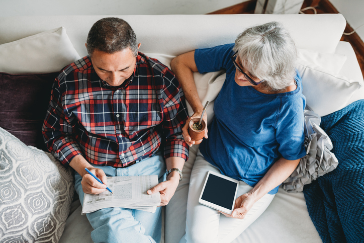 a senior couple sitting on the couch doing a crossword puzzle together