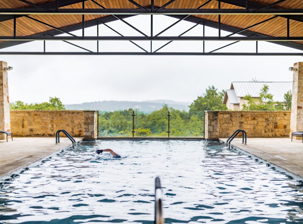 gorgeous outdoor lap pool at Querencia Senior Living Community, set in a stone lounge area covered by wooden roof, backdropped by mountains