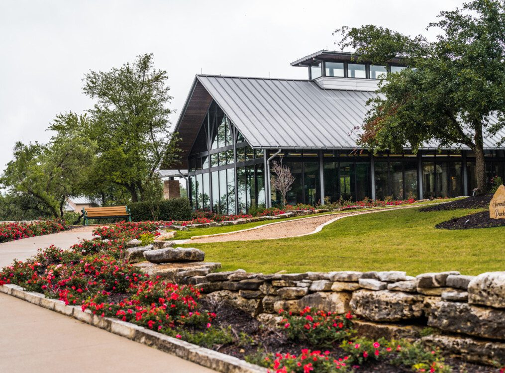lush landscaping along a driveway leading up to the glass fitness building at Querencia Senior Living Community in Austin, TX