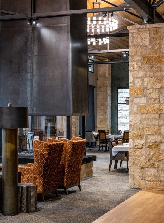 elegant and rustic-chic dining room and lounge at Querencia Senior Living Community featuring multiple tables and central fireplace