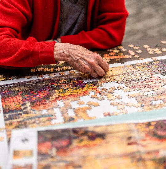 close-up of senior in red cardigan putting together a large puzzle
