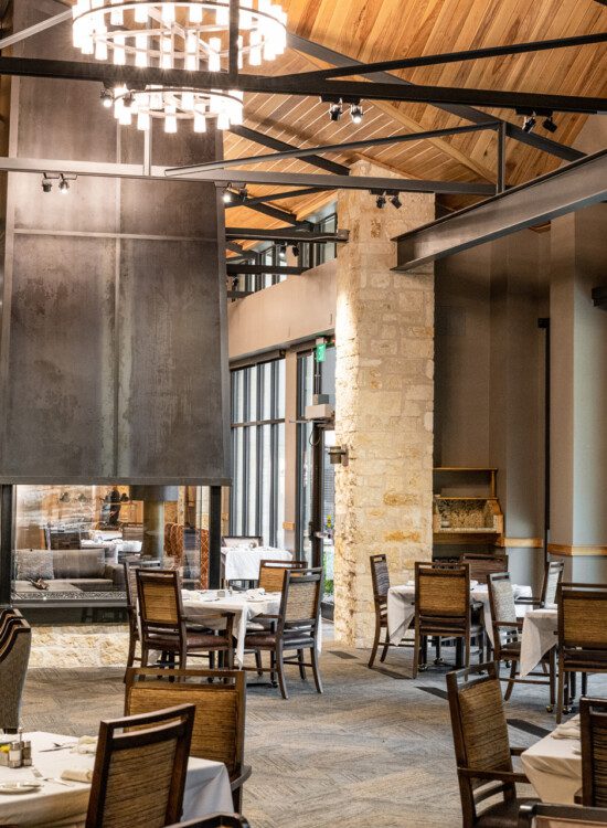 rustic-chic dining room area with vaulted ceilings, chandelier, and stone accents at Querencia Senior Living Community in Austin, TX