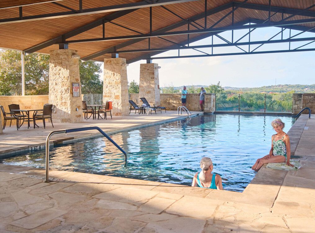 senior women lounge at the gorgeous outdoor pool at Querencia Senior Living Community enjoying drinks