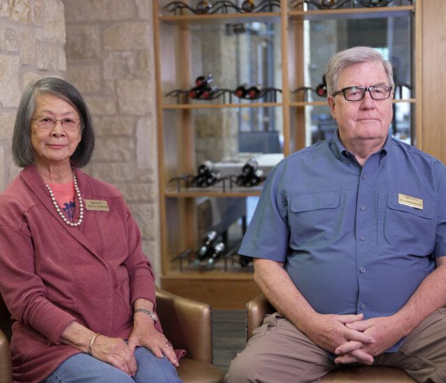 Well-dressed senior couple, the Sherwoods, sit smiling in chairs at Querencia Senior Living Community during an interview