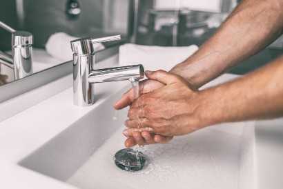 senior washing their hands with soap and water in a sink