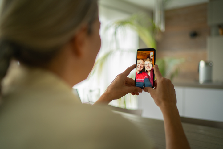 an elderly couple and their adult daughter speaking on a phone using video chat