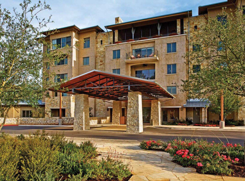 exterior view of the entrance and lush landscaping at Querencia Senior Living Community in Austin, TX