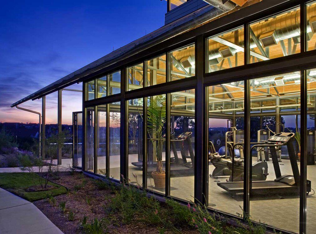 exterior view of glass-enclosed fitness center at night at Querencia Senior Living Community