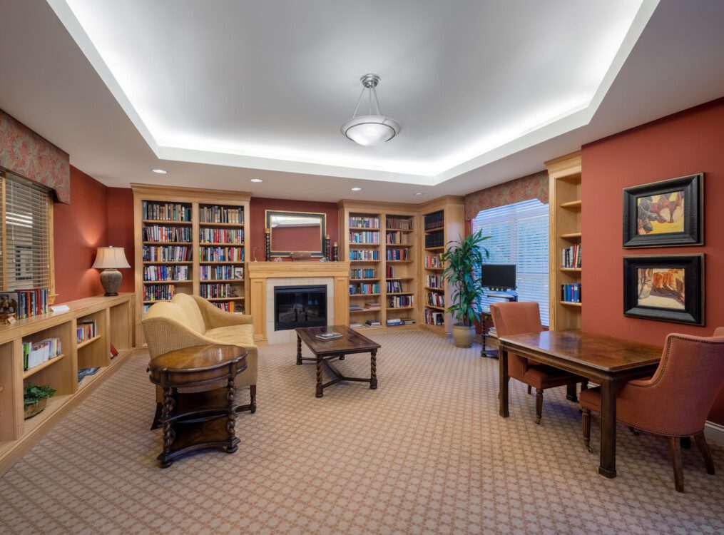 traditional lounge and library space with ample seating, electric fireplace, and built-in book shelves at Querencia's Assisted Living building