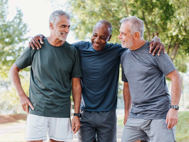 Three men smiling as they’re out for a walk in their senior living community.