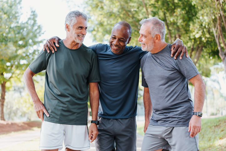 Three men smiling as they’re out for a walk in their senior living community.