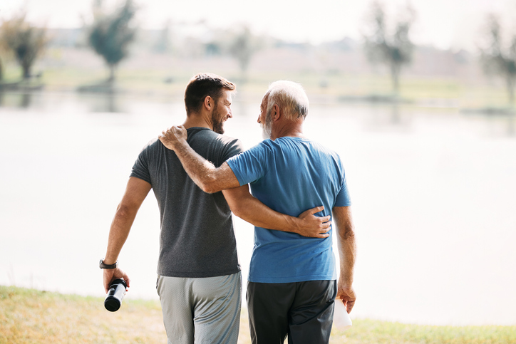 Senior father and adult son smiling as they walk together outside.